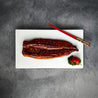 Unagi Kabayaki 500g topped with sesame seeds displayed on plate with herbs, cherry tomato, and a pair of chopsticks in Singapore (flatlay).